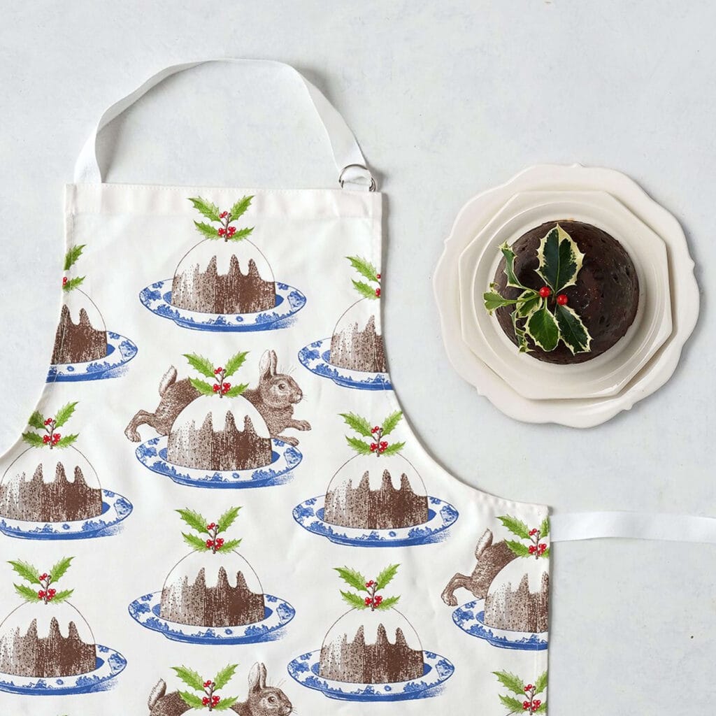 Apron decorated with Christmas puddings and a christmas pudding on a plate ext to it.