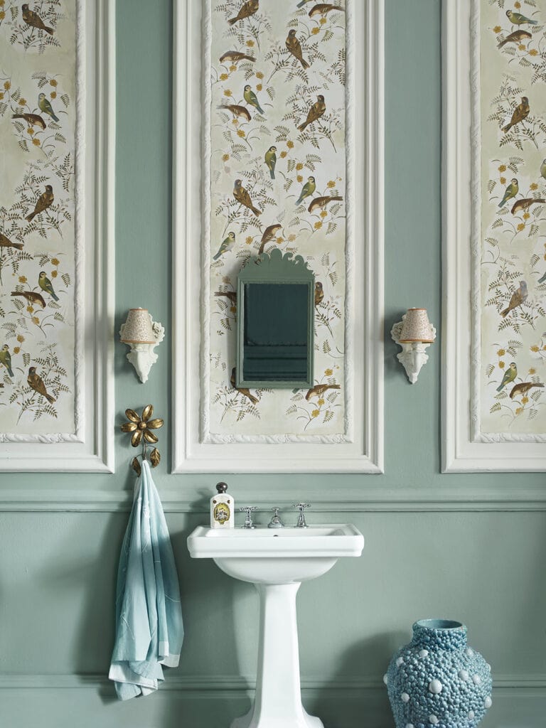 traditional white pedestal bathroom sink in front of green wall with panelling decorated with bird wallpaper above