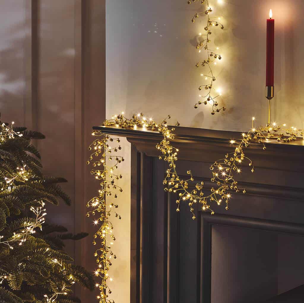Golden fairy lights draped across mantle with corner of christmas tree showing