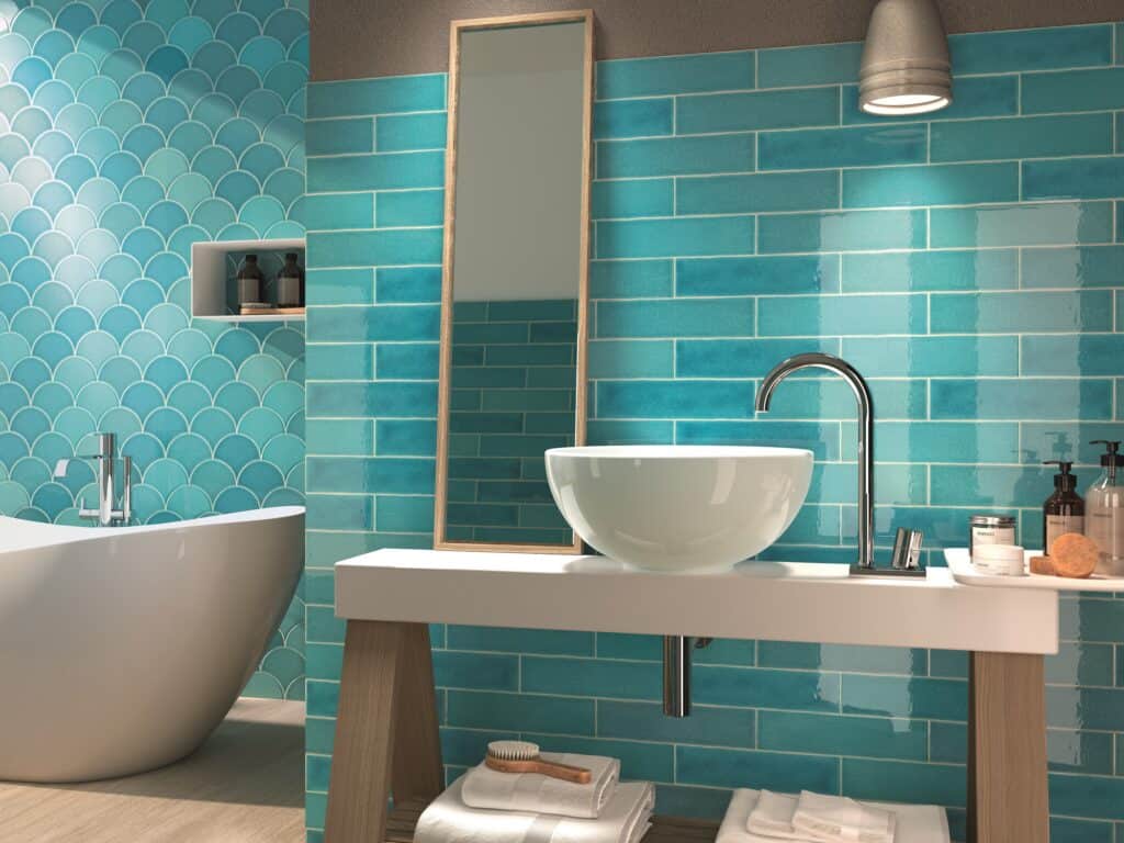 Turquoise bathroom tiles. In front of shot is a round basin, a bathroom shelf with towels underneath and a mirror propped on it. To the right is the corner of a free standing bath.