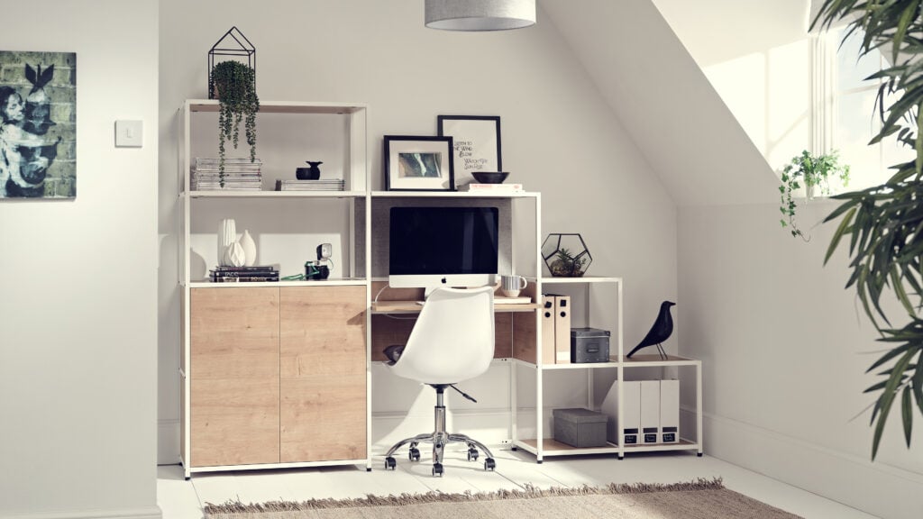 A home office set up with box shelving against a wall and an office hair in front sat. To the left is a window letting in lots of light.