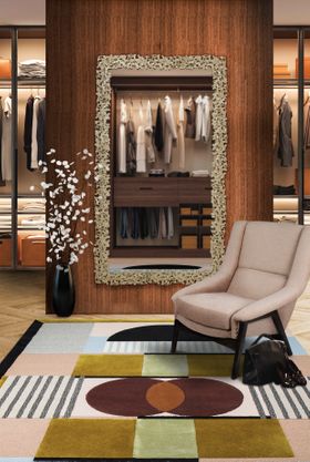 Mid century style sitting room with arm chair in foreground sat on geometric statement rug. Behind the armchair is hung a large mirror.