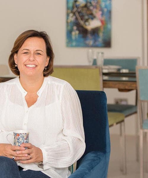 Joanne Jeyes, owner of Crocus Interior Design in Essex sitting holding cup of tea in front of modern dining room setting
