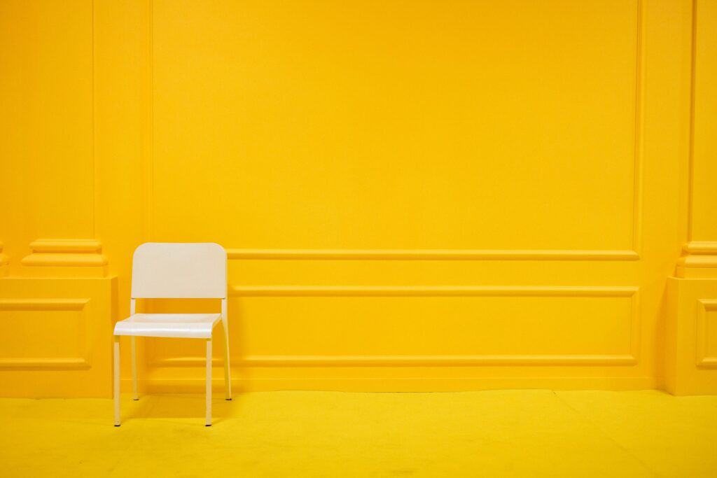 A bright, acid yellow wall and floor with a bright white plastic chair in front