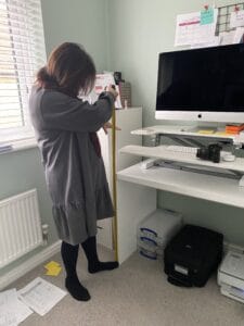 A lady wearing a grey dress is measuring an office desk using a tape measure.