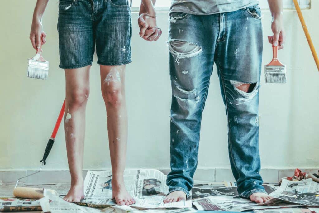 Bottom half two people, one wearing shorts, one wearing jeans. Both covered in paint