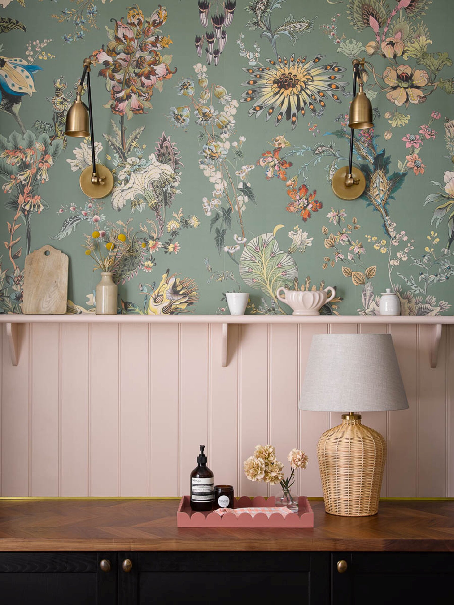 Green floral patterned wallpaper above pale pink panelling and wooden counter