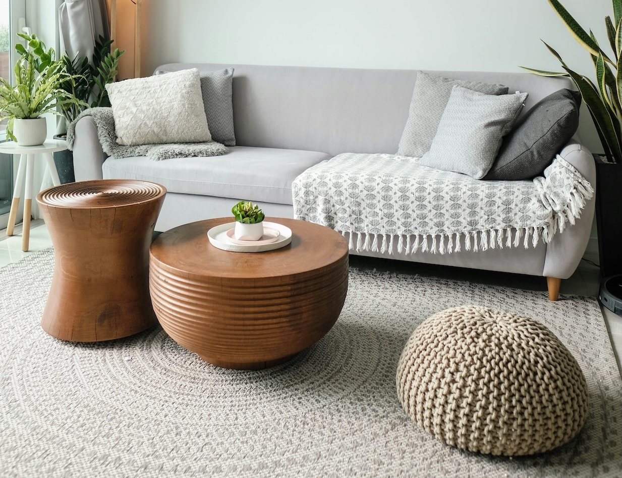 A sitting room in pale blue, grey sofa, with warm grey cushions and throws, grey curtains, plants on a table and two wooden coffee tables.